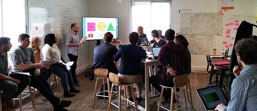 un groupe de personnes assises écoute un conférencier debout devant un écran